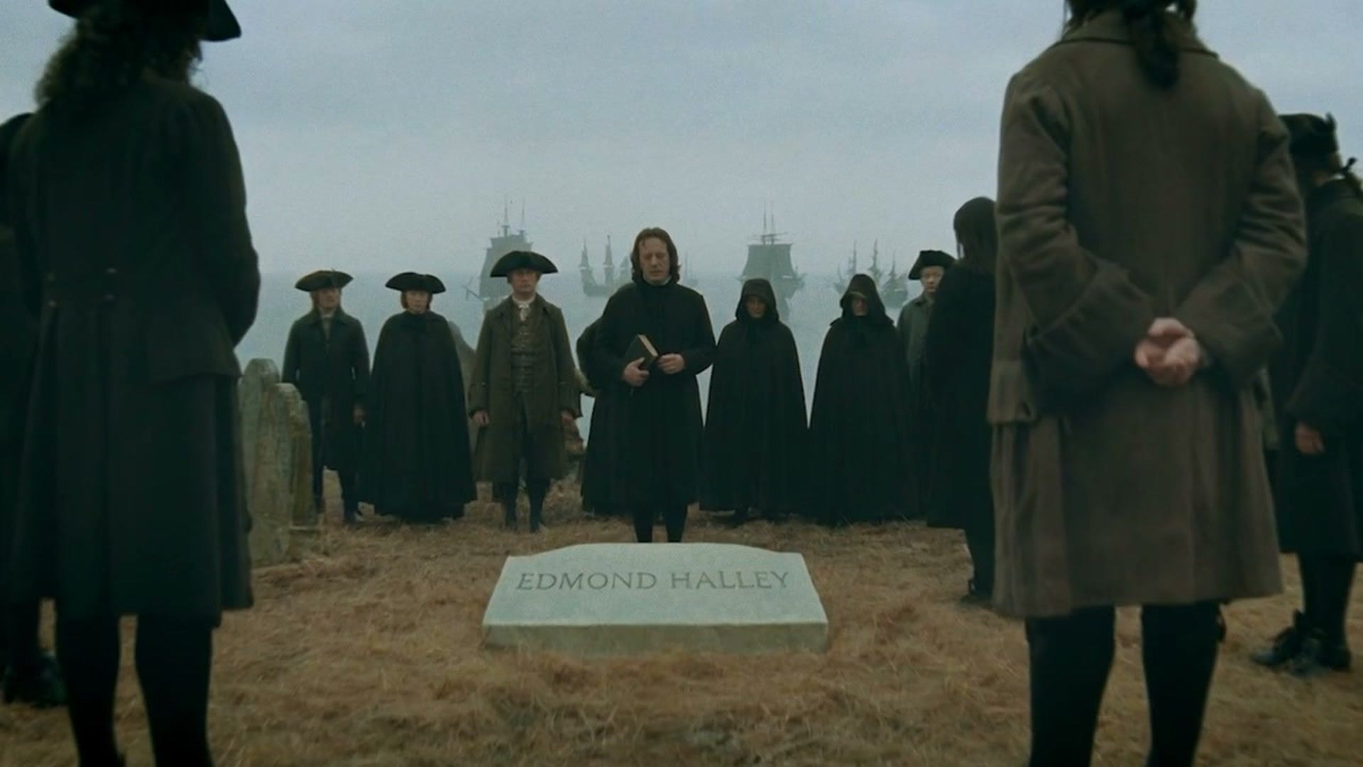 Mourners standing around Edmond Halley's grave on a headland while a fleet of tall ships lies at sea behind them