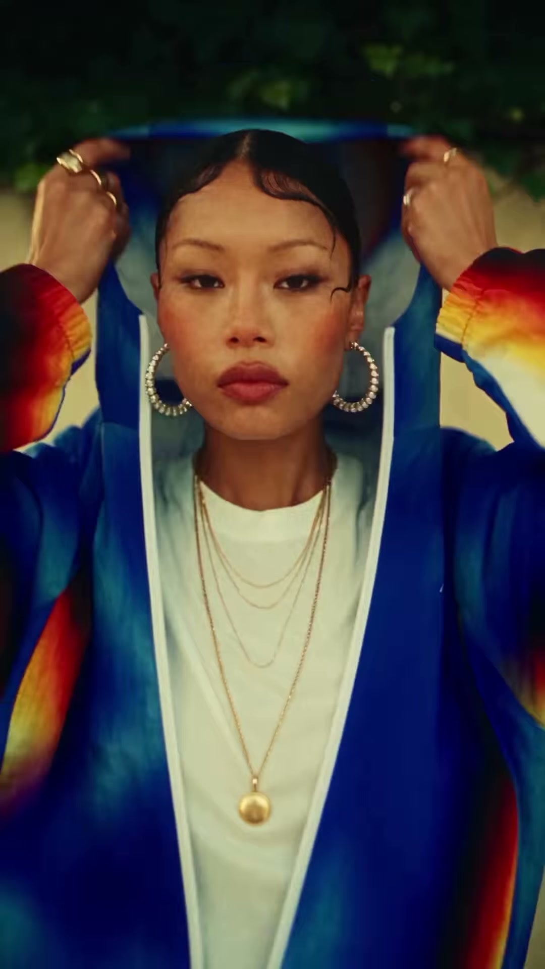 A woman pulls the hood of a blue Mertra jacket with flame-coloured sleeves over her head and looks straight into the camera in Jerry Oriadé's spec fashion film