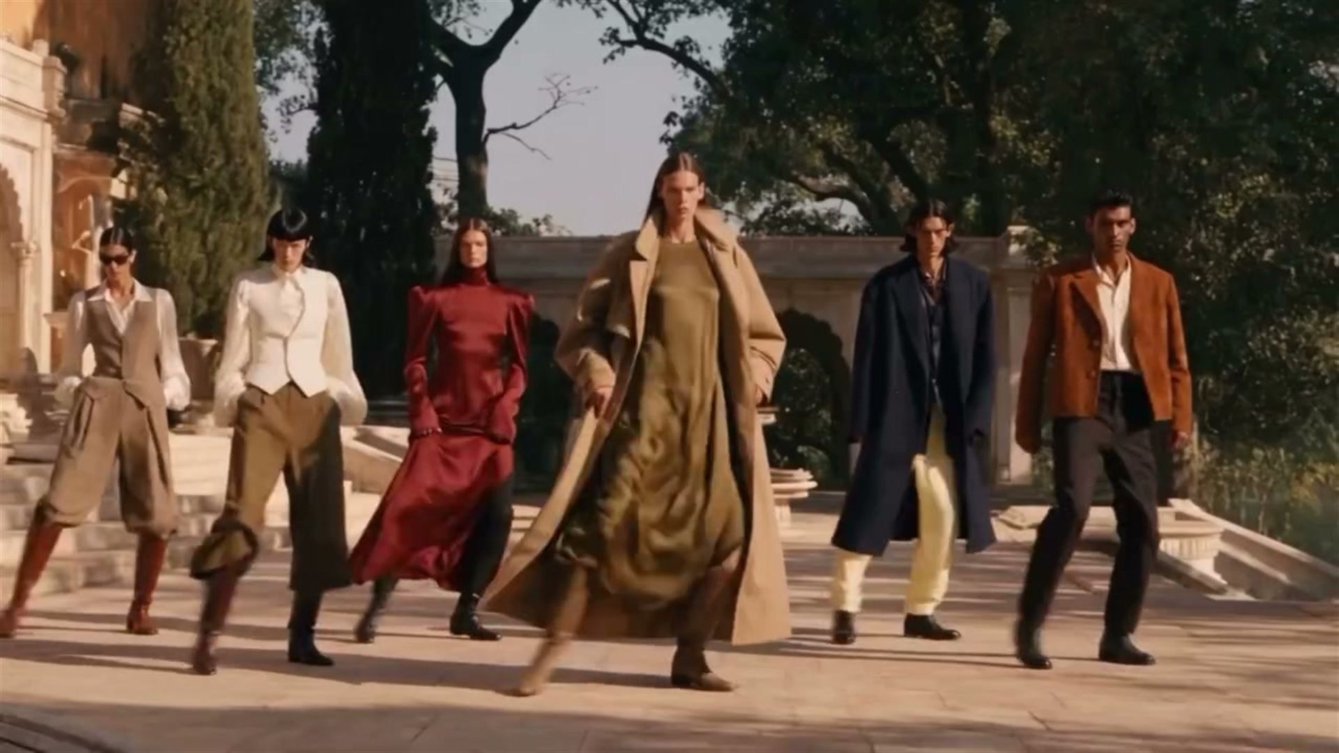 Six performers in tailored coats and period dress step in unison across the stone terrace of an ornate house in I / II / III Ecstacy, Then Nothing by Rahul Patil